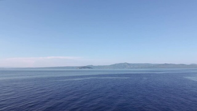 Drone flying revealing shot of fishing boat at calm sea in Greece. Aerial top view of caique sailing at Kassandra Chalkidiki peninsula shoreline with green plantation & background Sithonia view.