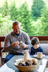 Father and son having breakfast with coffee and milk at table.Cute little boy and his father enjoying time together while having breakfast.Happy dad and son talking and smiling at the table. 