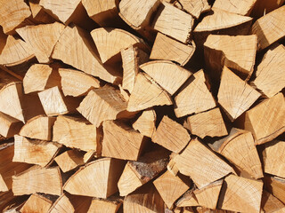 The background of stacked chopped firewood on a sunny day.
