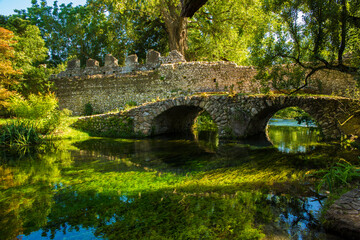 View of the Roman bridge of Ninfa, an ancient medieval town located in the province of Latina, Italy. Now it is part of the complex of Ninfa gardens. - obrazy, fototapety, plakaty