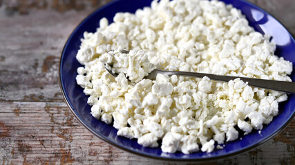 Selective focus. Freshly grained cottage cheese in a blue plate. Dairy products.