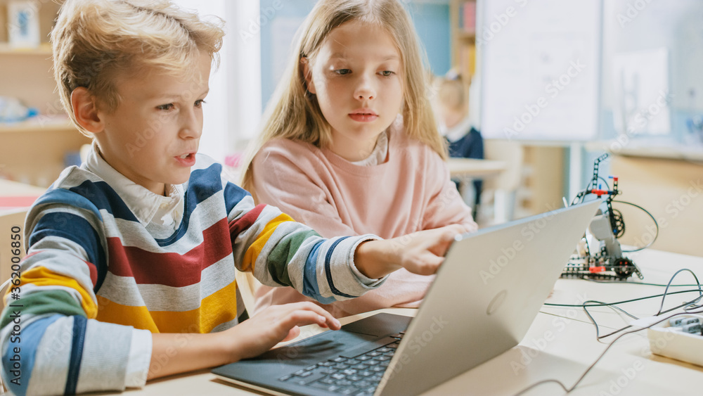 Poster brilliant schoolgirl and schoolboy talk and use laptop to program software for robotics engineering 