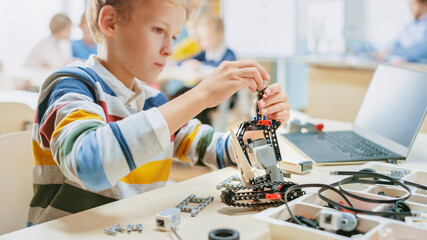 Schoolboy Builds / Constructs Small Robot and Uses Laptop to Program Software for Robotics Engineering Class. Elementary School Science Classroom with Gifted Brilliant Children Working with Technology
