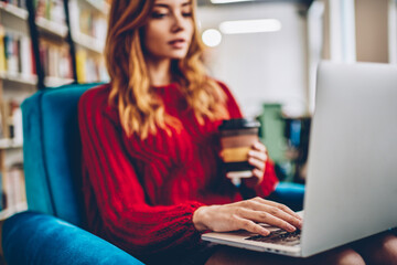 Selective focus on female hand typing text message via netbook device, young hipster girl browsing internet and searching language courses for studying online using laptop computer and wifi connection