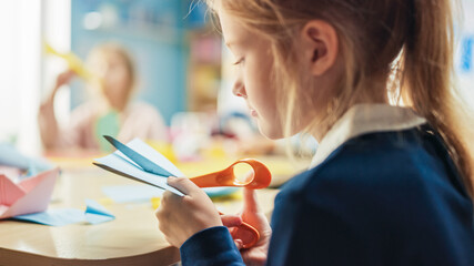Elementary School Arts & Crafts Class: Over Shoulder of a Girl Has Fun  on the Handicraft Project, Cuts Paper Figures with Scissors. Creative Young Girl