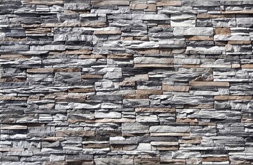 Stone cladding wall made of  striped stacked embossed natural rocks. Colors are gray, black, brown and white. 