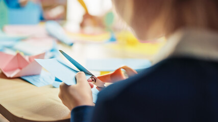 Elementary School Arts & Crafts Class: Over Shoulder of a Girl Has Fun  on the Handicraft Project, Cuts Paper Figures with Scissors. Creative Young Girl