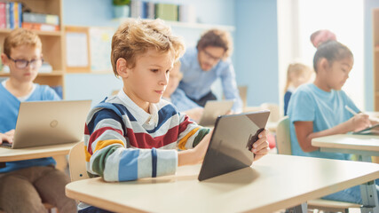 Elementary School Computer Science Class: Smart Boy Uses Digital Tablet Computer, His Classmates...