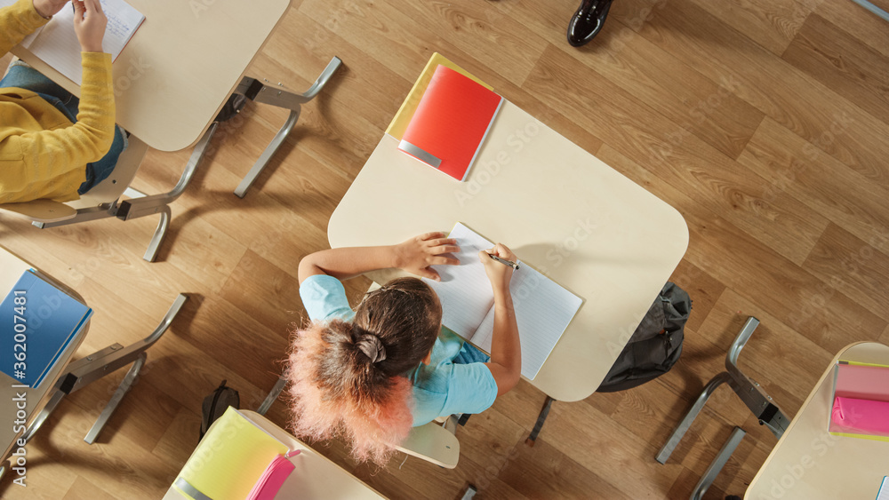 Aufkleber top view shot of elementary school classroom: girl sitting at the school desk working on assignments