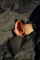 Woman's ear in hole in black crumpled paper background, black and white concept photography for...