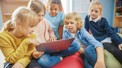 Diverse Group of Cute Small Children Sitting together on the Bean Bags Use Laptop Computer and Talk, Have Fun