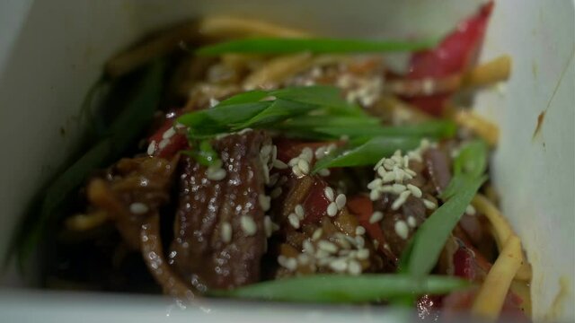 Close up of hand with chopsticks mixing noodle with meat and vegetables in paper box. Asian box food with chopsticks.
