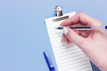 Important business checklist, planning for shopping reminder or project priority task list on blue background with copy space. Pen in female hands