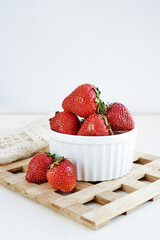 Close Up on Fresh ripe red strawberries in ceramic white bowl on rustic wooden stand with white background, natural food
