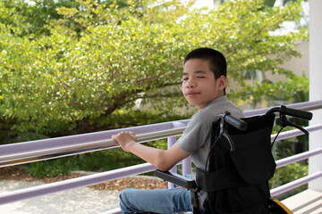 Asian special child on wheelchair is smile happily on ramp for disabled people background and orange light, Life in the education age of disabled children, Happy disabled kid concept.