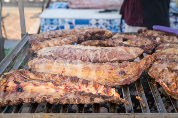 BBQ rack of pork ribs lined up on a large outdoor grill with smoke coming up from the fire below.