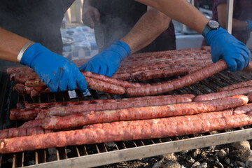 BBQ Sausage lined up on a large outdoor grill with smoke coming up from the fire below. person in...