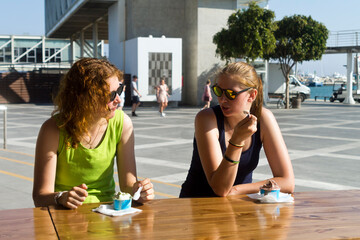 Two girls talking and eating ice cream in street cafe