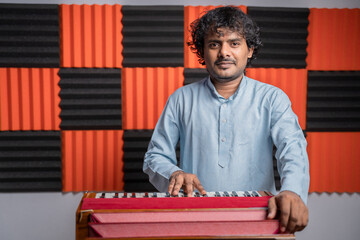 Young musician playing Indian music instrument Harmonium in studio.