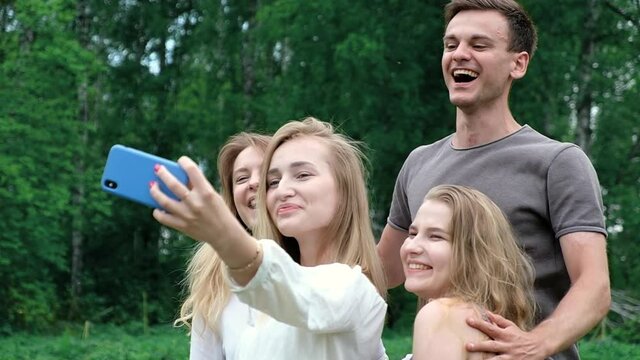 Friends have fun in the Park on a picnic making a group selfie. A man and a woman look at the camera, have fun and spend a happy vacation and weekend in nature together