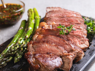 juicy, grilled, sliced beef steak, with roasted asparagus, close up, sauce