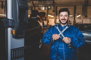 Fototapeta na wymiar Positive auto mechanic stands with wrenches in his hands. Car service concept
