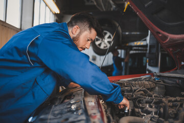 Male auto mechanic in blue uniform is repairing a car