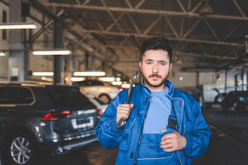 Portrait of a car mechanic who holds wrench on his shoulder. Auto mechanic in the garage