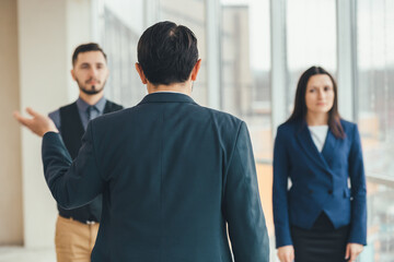 Angry boss standing back to the camera, shouting at his workers, raising hand, while stressed...