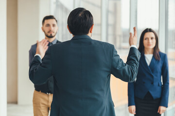 Angry boss standing back to the camera, shouting at his workers, raising hand, while stressed...