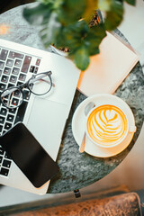 cup of coffee with latte art on the table with coffee plant and menu, mockup, laptop, glasses