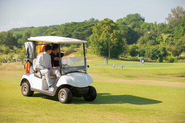 Two asian man golfer driving golfcar on road in golf course