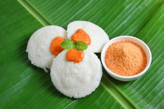 Many Idli or idly with coconut chutney powder popular breakfast of South India and Sri Lanka arranged on banana leaf. Healthy steamed cakes made by steaming fermented batter of black lentils and rice 