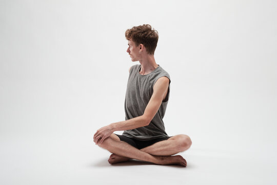 Young boy meditating with his body turned to his right and legs crossed on white background