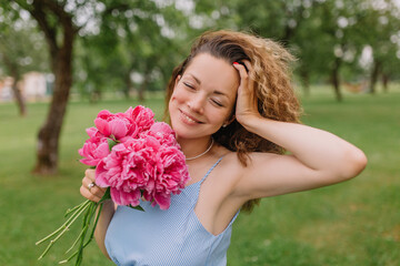 Fototapeta premium girl model mother on her head curly curls holding peonies and flowers in her dress gently presses them to herself on the nature in the park