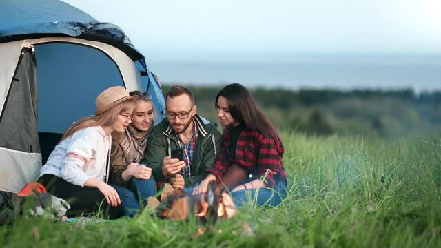 Cheerful guy showing photo on mobile to happy girls surrounded by nature. Wide shot on RED camera