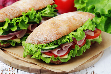 Two sandwiches with fresh vegetables, ham and cheese in ciabatta bread	