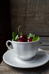 Sweet cherries in a white tea cup on wooden rustic background