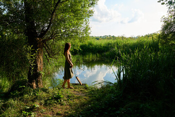 A girl stands at the lake on a sunny summer day in Russia.