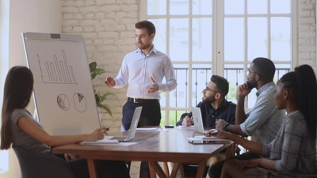 Serious businessman manager presenter speaker give flip chart business presentation explain statistics work result speaking to diverse employees group teach team at office meeting workshop training.