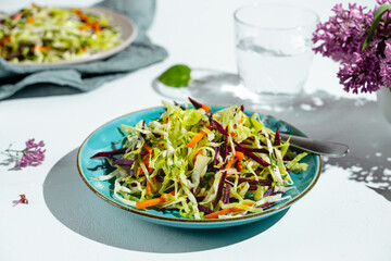 Blue plate with coleslaw salad with purple and orange carrots, glass of pure water on white background, closeup view