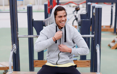 Portrait of a happy smiling sportsman having a break after workout outdoors, jogger man listening to music in headphones enjoying rest,young sporty guy rest after training sitting on sports ground.