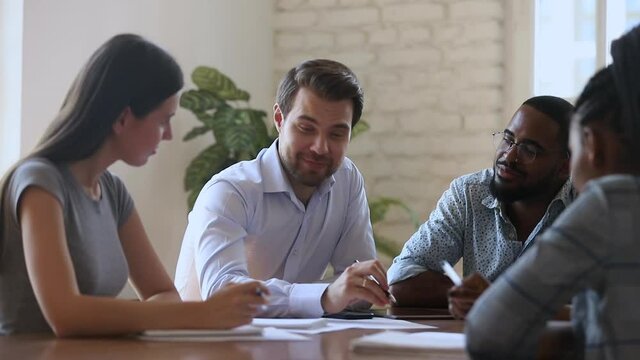 Smiling male boss leader mentor and diverse business team laugh discuss paperwork planning project at group office briefing, happy multiracial staff talk work together joking sit at meeting table