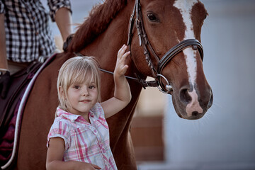 Beautiful little blonde girl with a big red horse