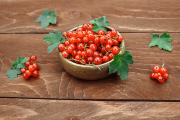 Berries of ripe, red and juicy currants in a wooden bowl with green leaves on a brown wooden table close-up, the concept of vitamin berries and pie filling