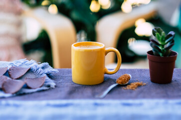 Hot coffee in yellow ceramic cup, outdoor on balcony with plants and chairs - defocused chocolates and sugar cane  on background