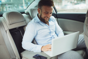 Young businessman working on laptop inside a car. A young businessman prepares for a meeting.