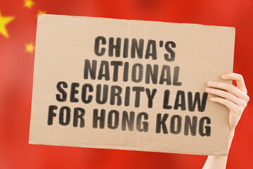 The phrase " China’s national security law for Hong Kong " on a banner in men's hand with blurred Chinese flag on the background. Politics. Illegal actions. Democracy. Unlawful. Freedom. Legislation