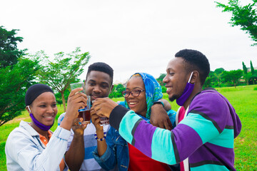 young black people standing in a park, giving a toast with drink in their glass cups