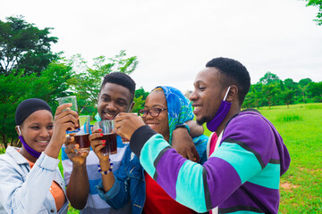 young black people standing in a park, giving a toast with drink in their glass cups